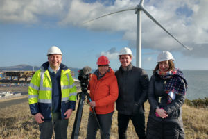 Group of people in hard hats standing in front of a wind turbine