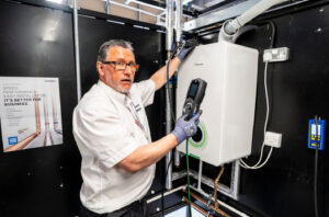 Engineer wearing a white shirt, standing in front of a gas boiler